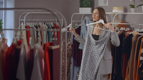 Estilo-De-Moda-De-Compras-Y-Concepto-De-Personas---Mujer-Feliz-Eligiendo-Ropa-Y-Mirando-Al-Espejo-En-El-Centro-Comercial-O-Tienda-De-Ropa